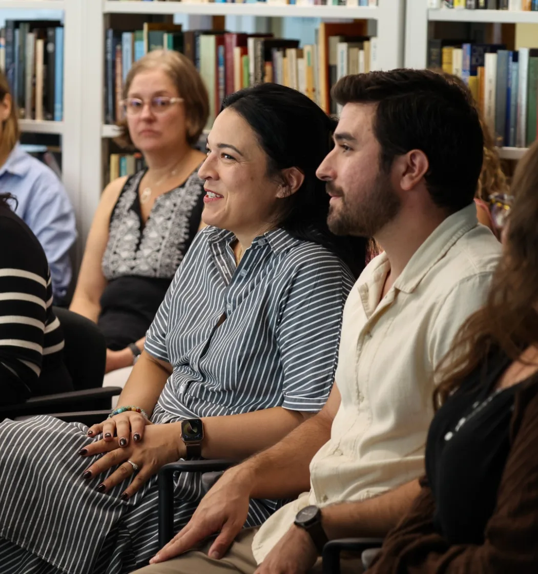Participants smile during a group discussion, seated in a circle in front of library bookshelves