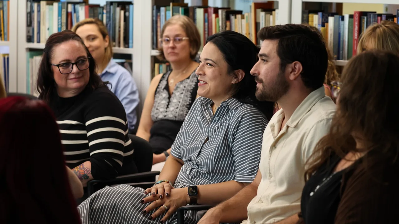 Participants smile during a group discussion, seated in a circle in front of library bookshelves
